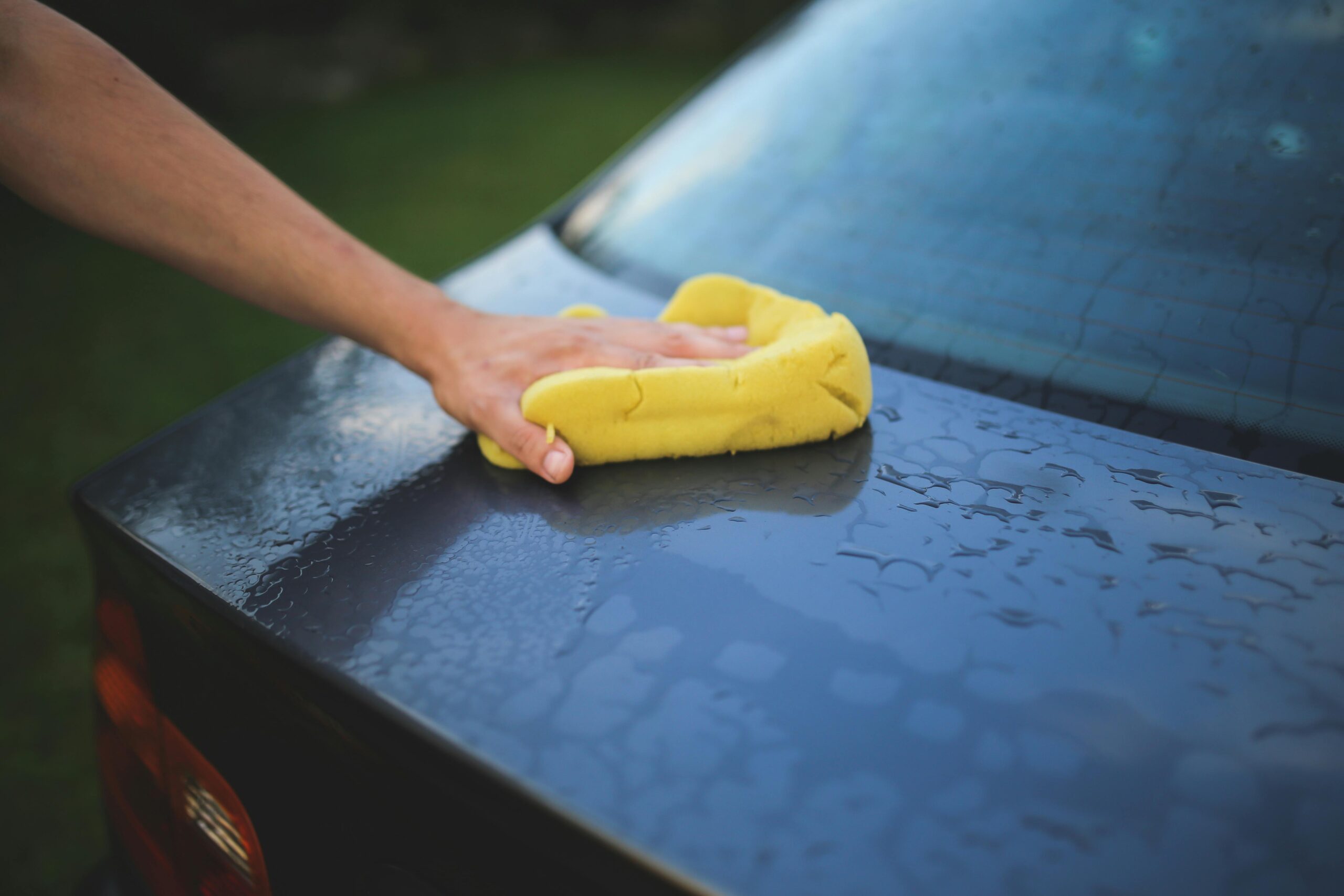 Hand cleaning car with a yellow sponge, showcasing car detailing and washing process.