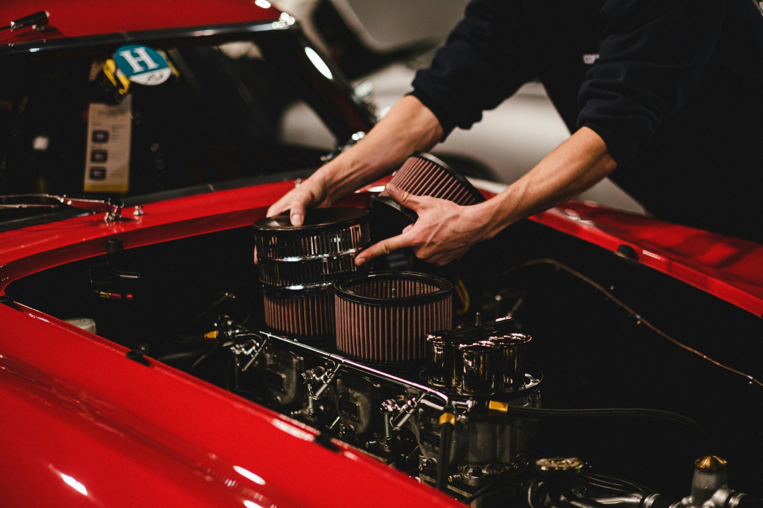 Close-up of a mechanic installing air filters on a classic red car's engine inside a garage.